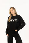 Close-up of black NYC sweater with white embroidery, paired with black wide-leg pants