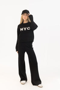 Model wearing Lyla + Luxe Yassie NYC black sweater with white lettering, paired with black PICO pants. Photographed at Lemonberry in Aurora, ON.