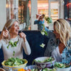 Two women enjoying fresh, vibrant salads made from recipes in Mandy’s Gourmet Cookbook, emphasizing the fun and social aspect of healthy eating.
