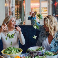 Two women enjoying fresh, vibrant salads made from recipes in Mandy’s Gourmet Cookbook, emphasizing the fun and social aspect of healthy eating.

